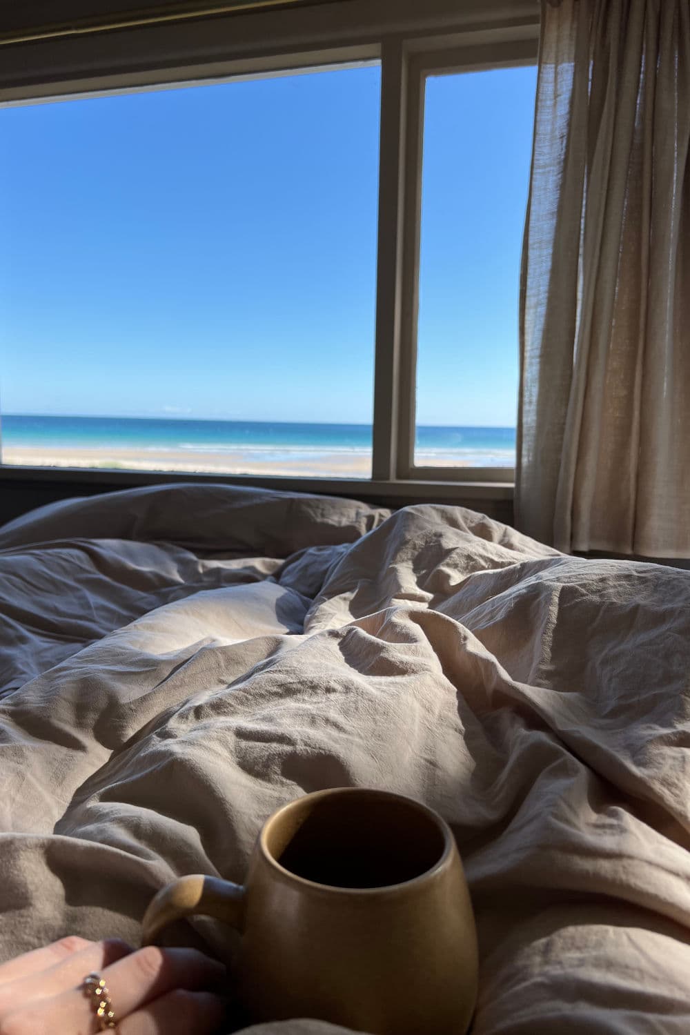 Lying in bed looking out over ocean with coffee in hand